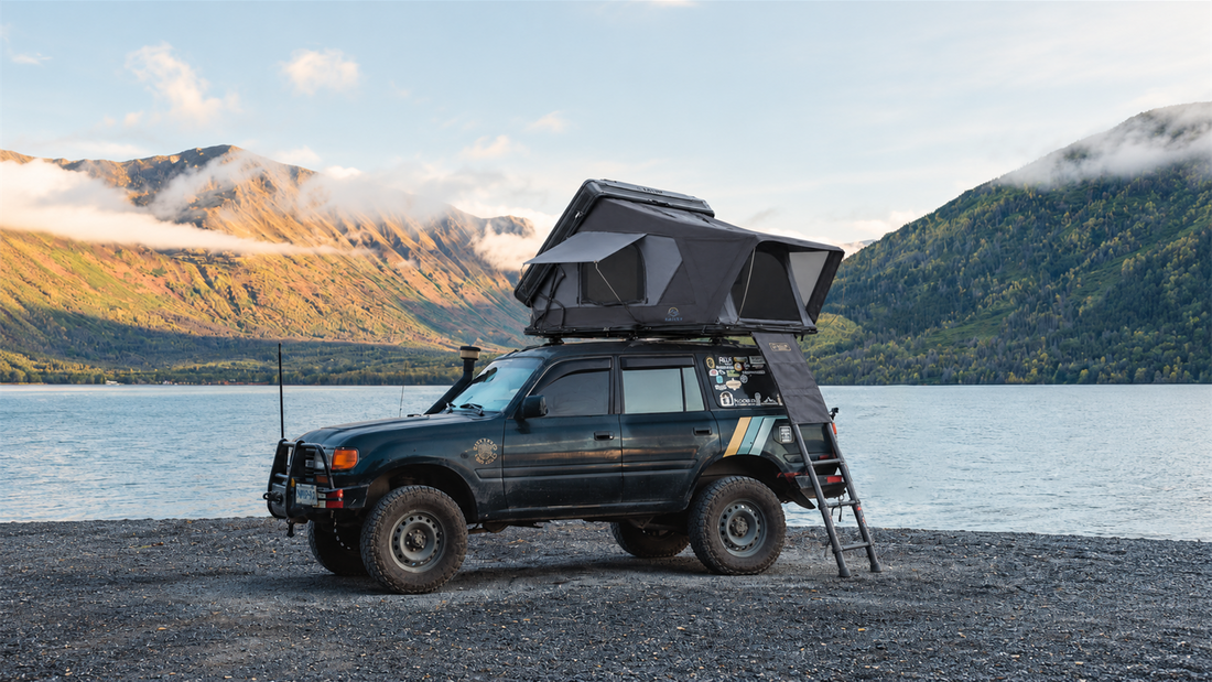 Tente de toit KAILOP déployée sur un SUV au bord d'un lac, avec des montagnes en arrière-plan.